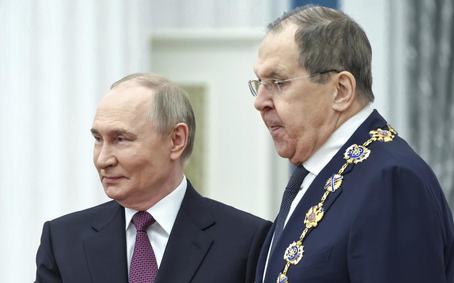 Vladimir Putin on the left next to Sergey Lavrov, who is seen from the side with awards attached to his suit.