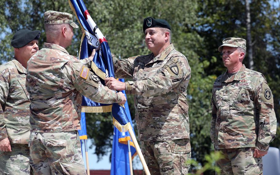 U.S. Army Gen. Christopher Cavoli, left, the head of U.S. European Command, passes the organizational colors to incoming commander Brig. Gen. Joseph Lock during the Special Operations Command Europe change of command ceremony July 15, 2024, at Patch Barracks in Stuttgart, Germany. At right is the outgoing commander, Air Force Maj. Gen. Steven Edwards.