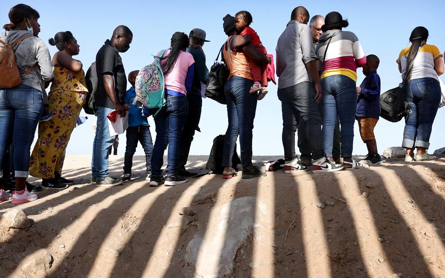 Immigrants from Haiti, who crossed through a gap in the U.S.-Mexico border barrier, wait in line to be processed by the U.S. Border Patrol on May 20, 2022, in Yuma, Ariz.
