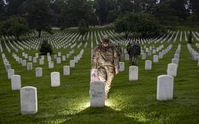 An Old Guard soldier prepares to place a flag in front of a headstone.