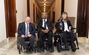 Three people in wheelchairs in a hallway.