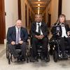 Three people in wheelchairs in a hallway.