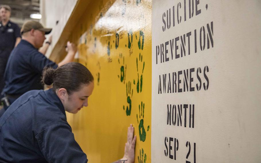 Petty Officer 2nd Class Alexis Vazquez places her handprint on the bulkhead of a vehicle stowage ramp during a suicide prevention event on the USS Green Bay, in the East China Sea, Sept. 29, 2021. Long family separations and lack of mental health support may put deployed and overseas service members at increased risk of attempting suicide, a new government report says.