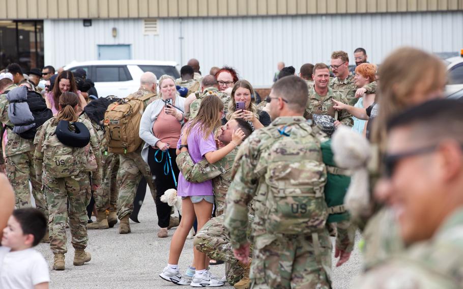 Soldiers in uniform embracing and smiling next to loved ones.
