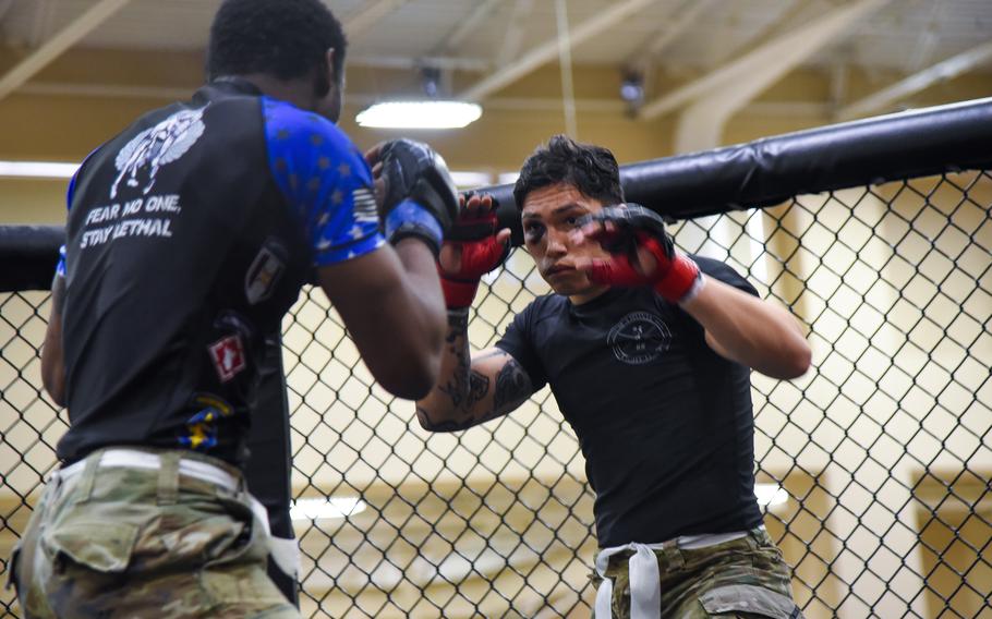 Two fighters face off in a cage, both with their arms raised.