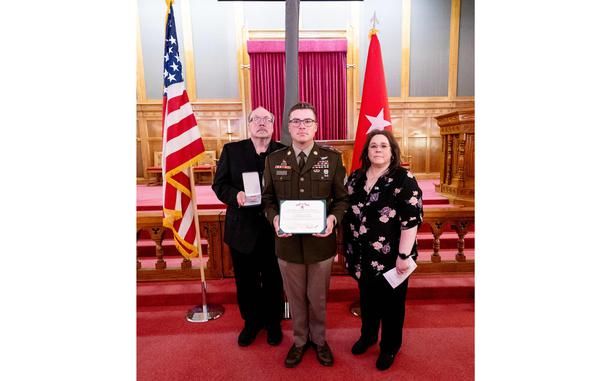 Martin and his parents hold the medals with flags behind them.