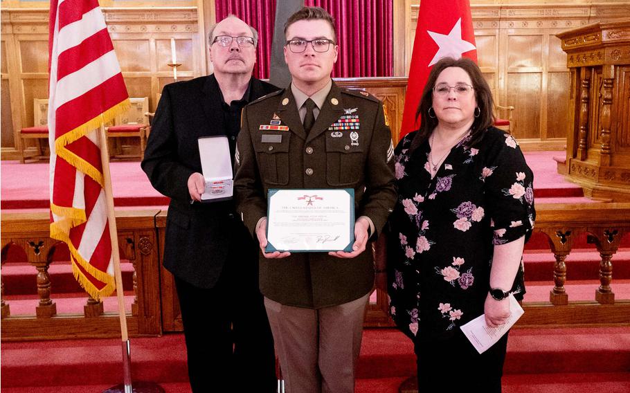 Martin and his parents hold the medals with flags behind them.
