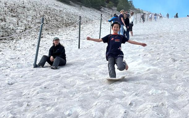 A smiling child runs down a hill made of sand.