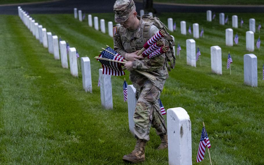 A soldier with multiple flags prepares to place one in front of a headstone.