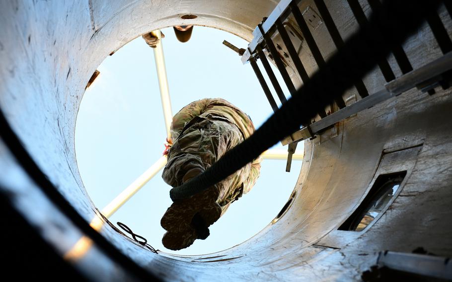 An airman climbs down a personnel access shaft on a rope.