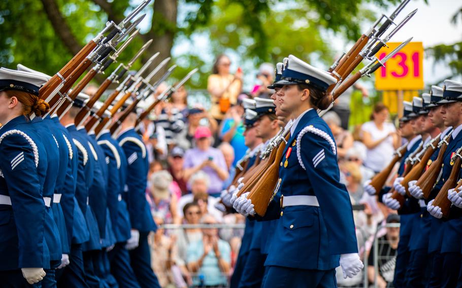 Soldiers in blue uniforms with guns on their shoulders march in formation.