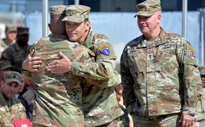 Two generals hug and another looks on during a change of command ceremony.