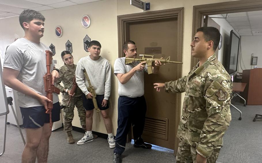 An airmen gestures towards a room as he instructs other airmen holding plastic weapons.
