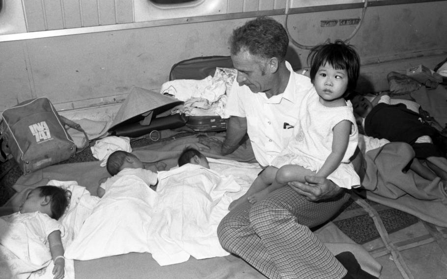 Three infants sleep while being watched by a sitting man, who is holding one toddler on his lap.