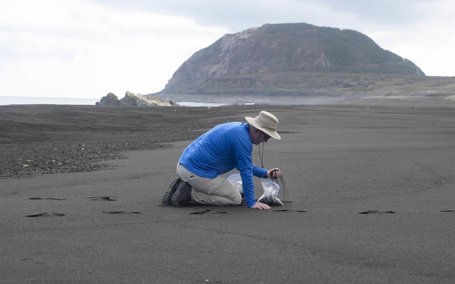 A U.S. airman from Kadena Air Base, Okinawa, collects sand from Invasion Beach on Iwo Jima, April 20, 2022.