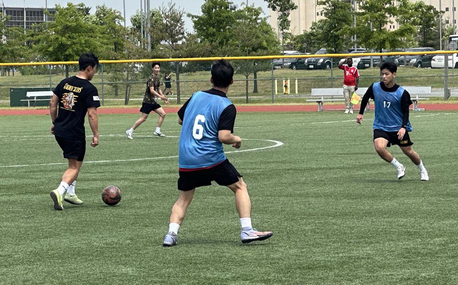U.S. and South Korean soldiers in exercise clothing kick a soccer ball on a grass field.