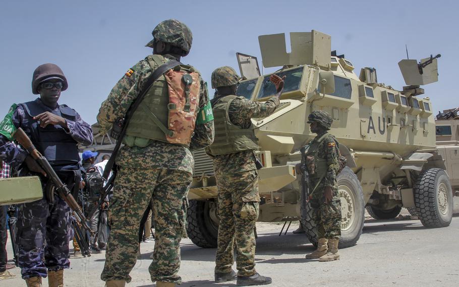 Peacekeepers in military fatigues stand by an armored vehicle.