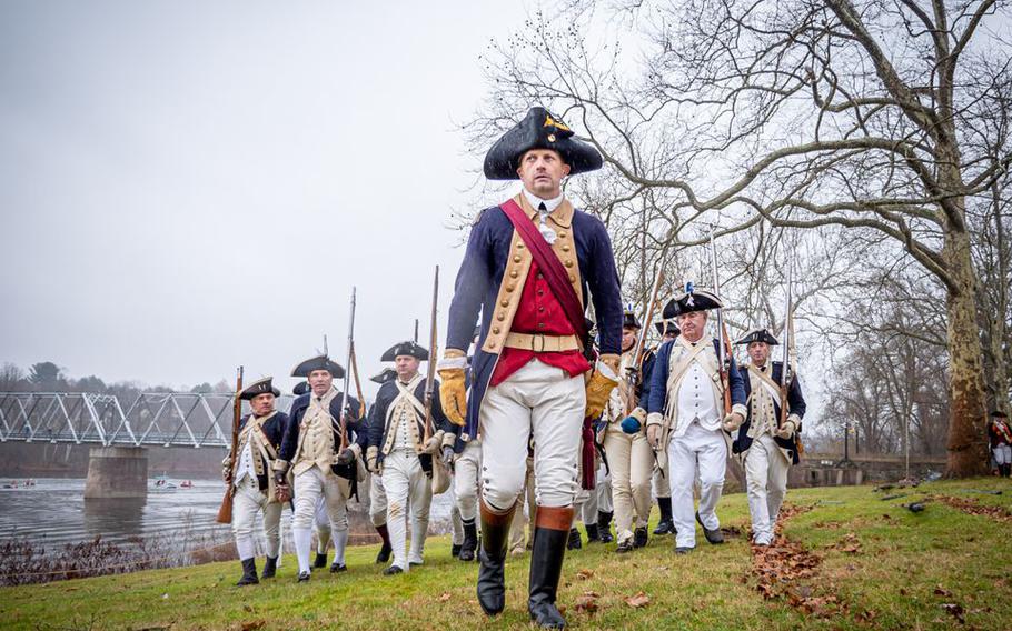 Men dressed as Revolutionary War soldiers march towards boats ready to cross the Delaware River during a Washington Crossing reenactment in Washington Crossing Pennsylvania on Sunday, December 11, 2022.