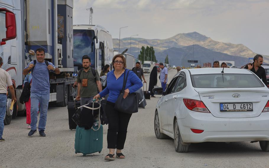 A woman pulls a suit case on a road with cars.