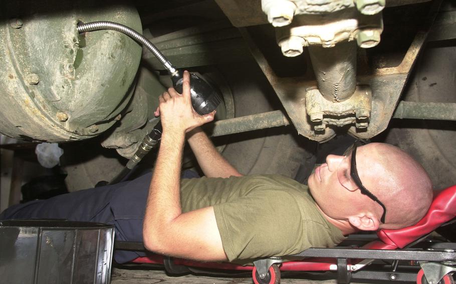 A Marine pumps fluid into a military vehicle while laying down