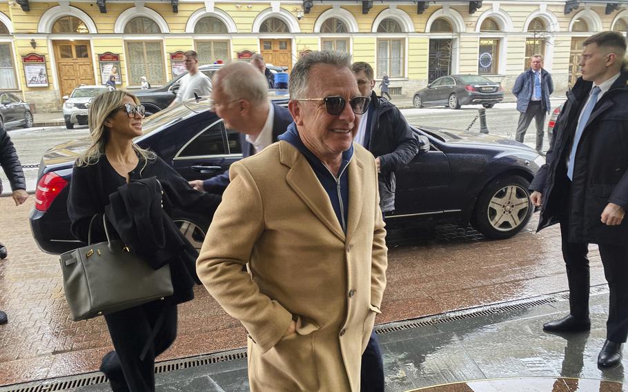 A man in a tan coat walking with both hands in his pockets.