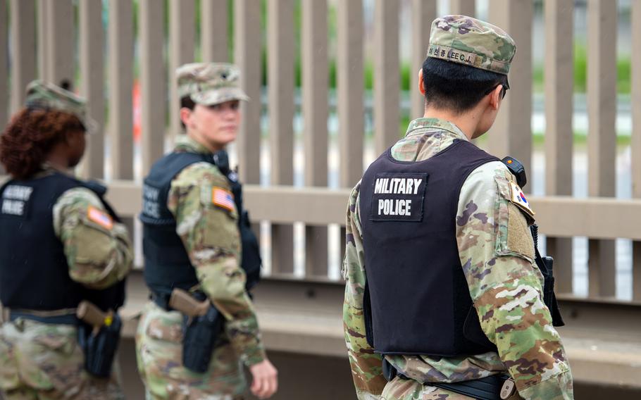 Military police personnel in camouflage uniforms and tactical vests stand guard. 