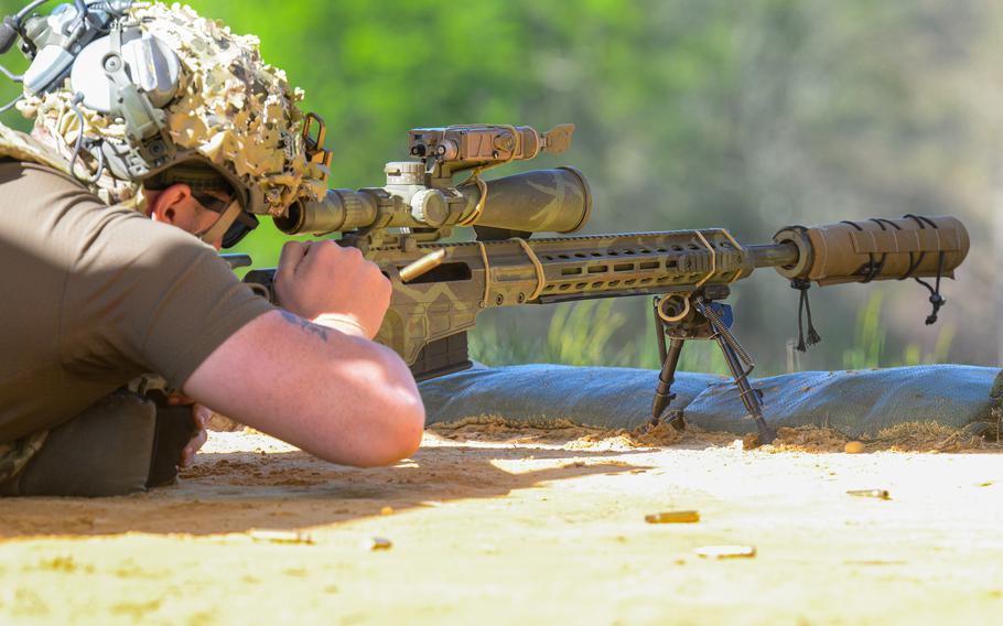 A sniper in a t-shirt aims down his camouflage rifle.