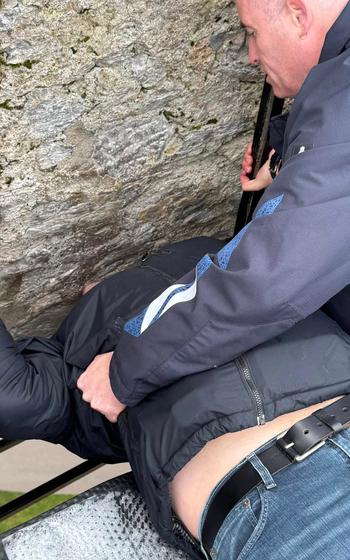 Man assisting another person while he arches his back to kiss the Blarney Stone