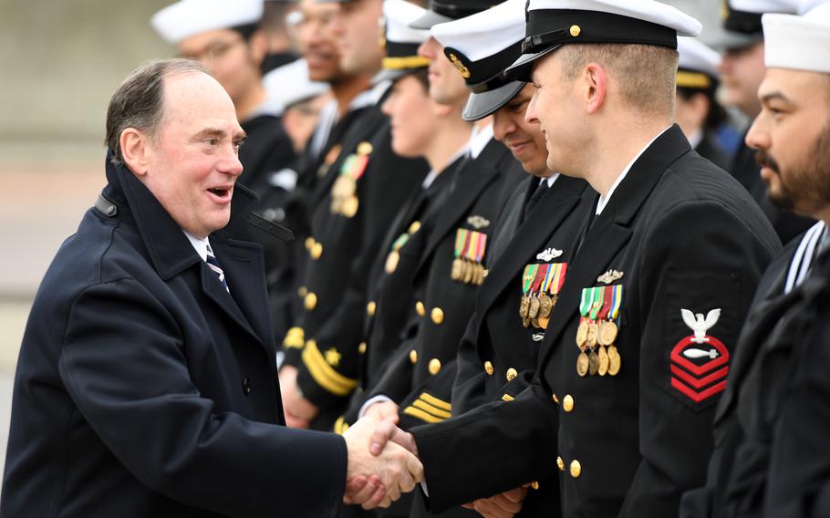 Secretary of the Navy John Phelan shakes hands with a sailor and smiles