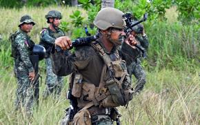 A Marine in the foreground walks through a field with Philippine marines in the background during Balikatan.