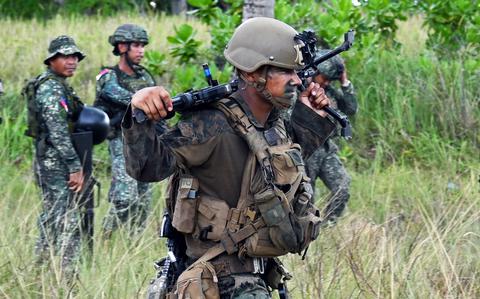 A Marine in the foreground walks through a field with Philippine marines in the background during Balikatan.