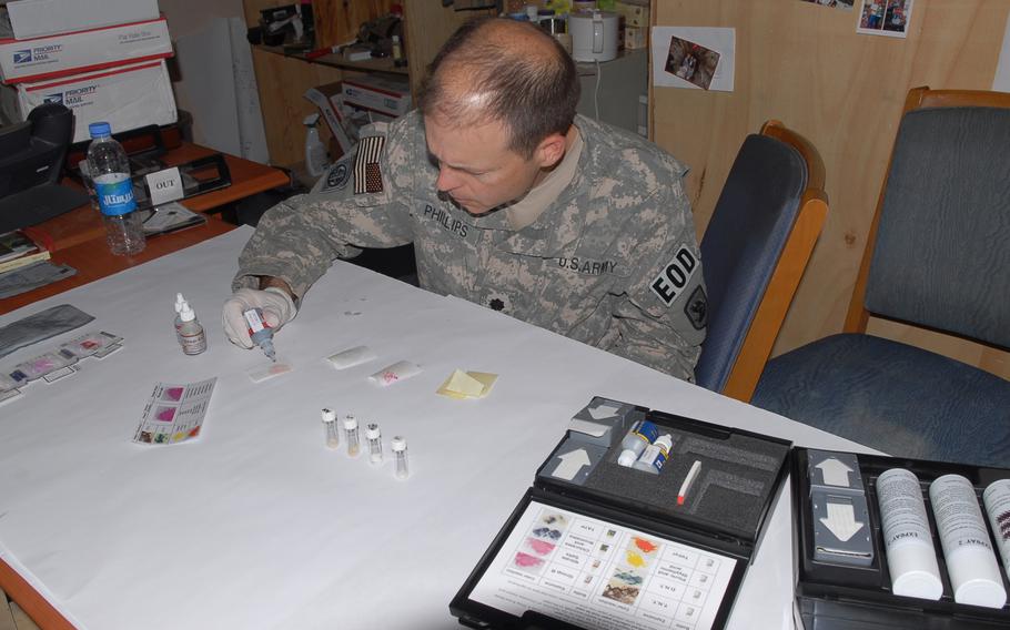 A service member seated and scientifically examining items on a table with medical gloves on.