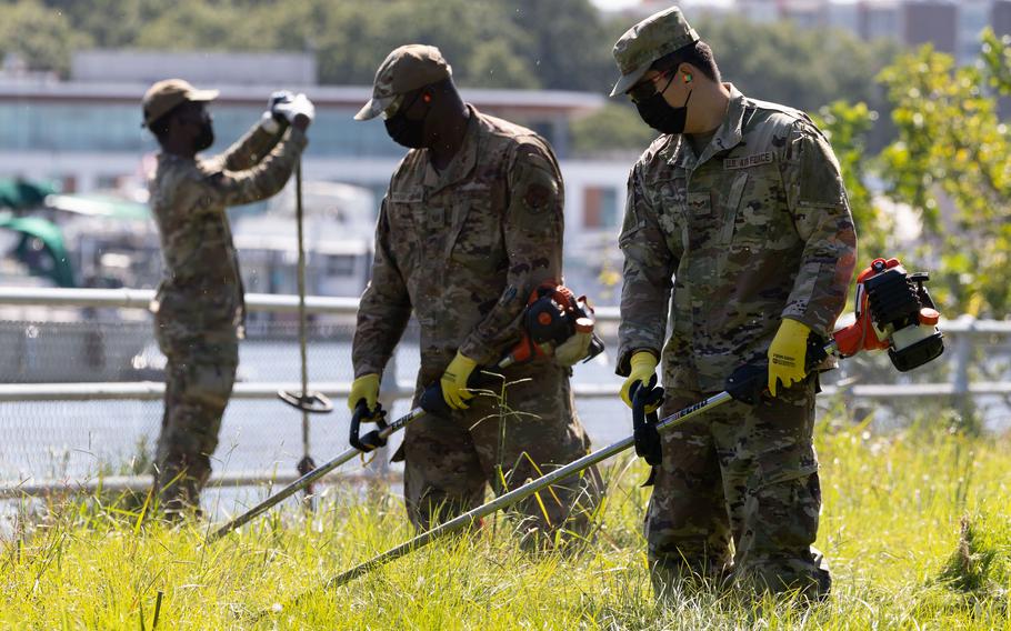 Soldiers cutting grass while wearing masks.