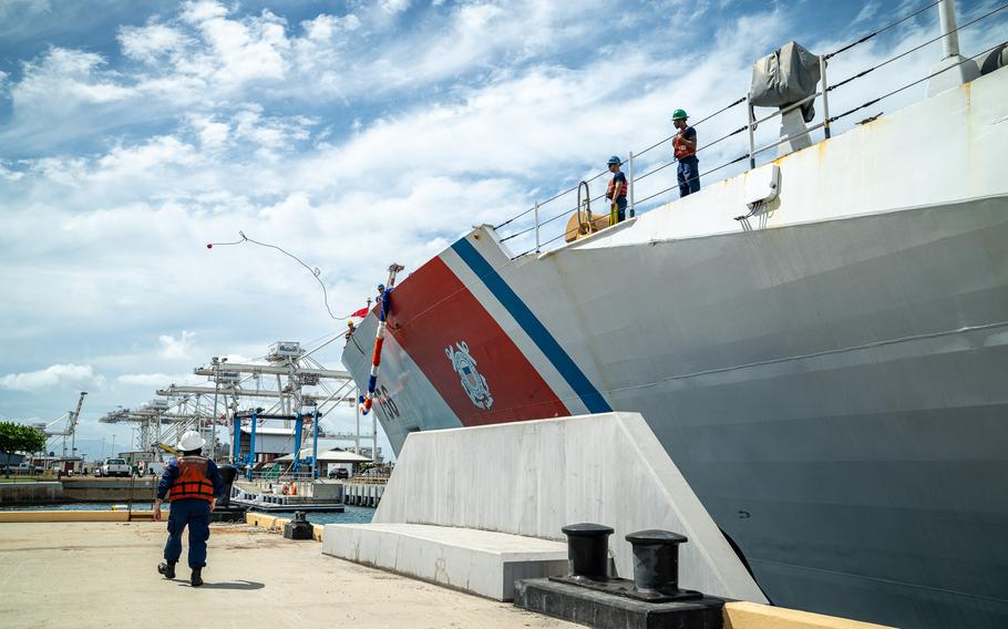 Coast Guard ship at a pier with two men on the ship and one on the pier.