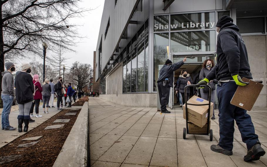A line for rapid coronavirus tests stretches around the block outside the Shaw Neighborhood Library in Washington on Dec. 30, 2021, as a delivery worker brings in more test kits.