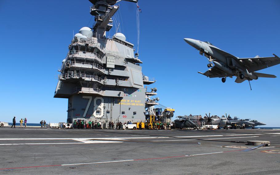 A fighter jet flies just about the deck of an aircraft carrier.