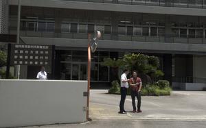 Two men speak to each other while standing outside a Japanese government building.