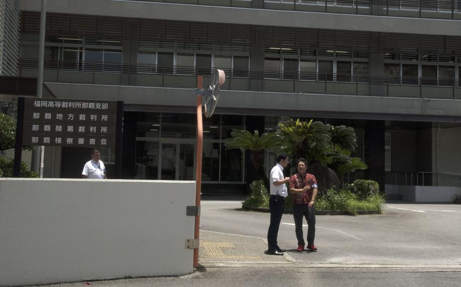 Two men speak to each other while standing outside a Japanese government building.