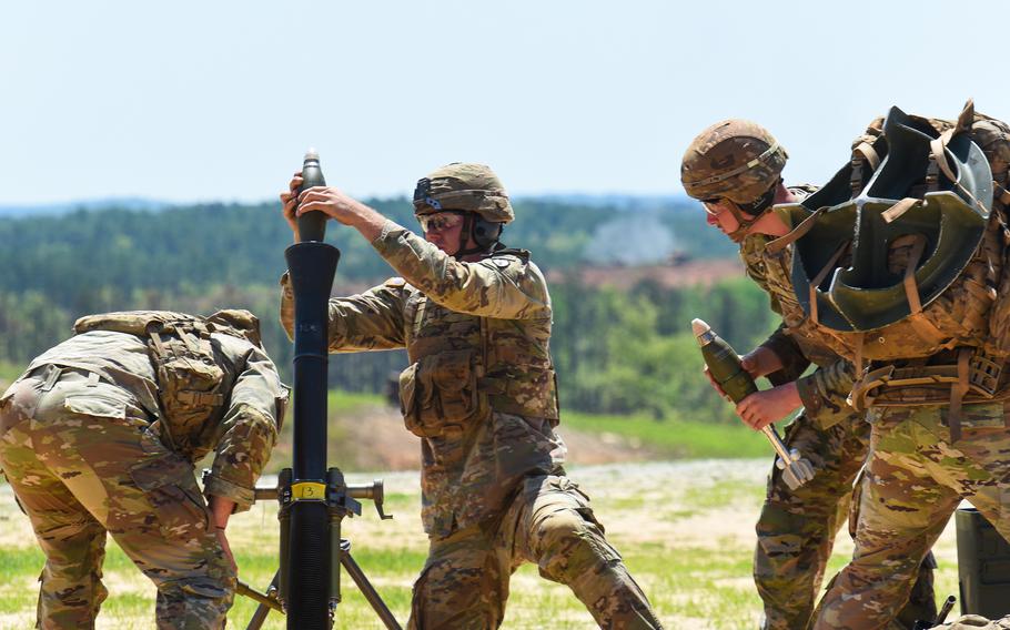 Four soldiers during the mortar competition. One drops a shell into the mortar, and second soldier carries a shell.