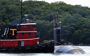 A submarine’s hull emerges from the water next to another ship.