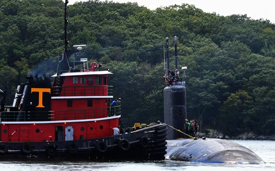A submarine’s hull emerges from the water next to another ship.