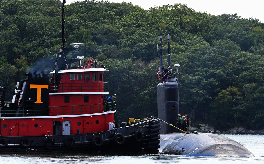 A submarine’s hull emerges from the water next to another ship.