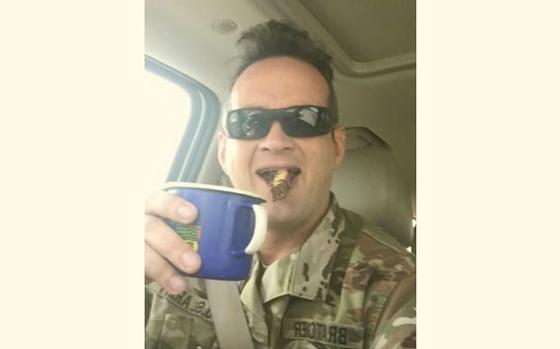 A vertical photo of a man in uniform taking a selfie and raising a blue cup to the camera.