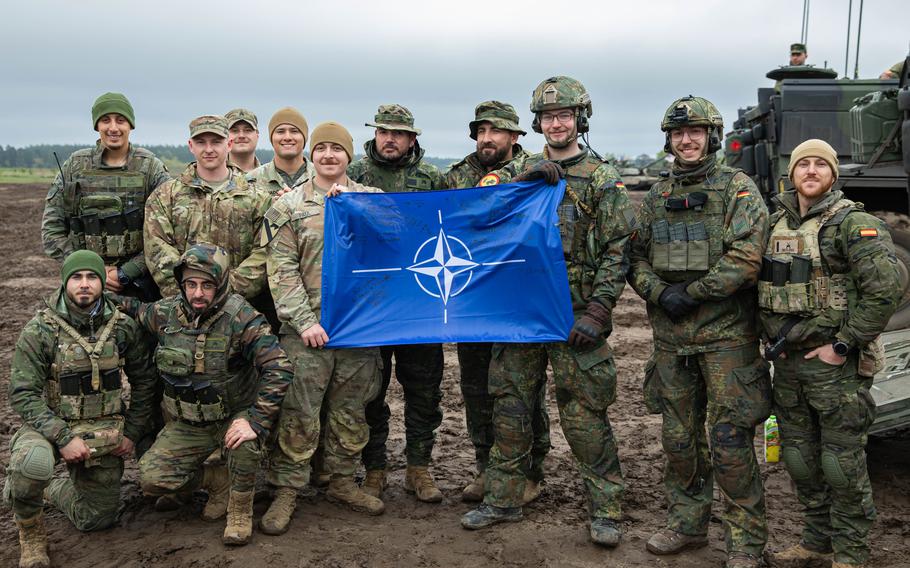 U.S. soldiers pose with service members from the German and Spanish armies holding the NATO flag during the Saber Strike exercise at Bemowo Piskie, Poland, in April 2024. NATO will mark its 75th anniversary at a summit in Washington, D.C., this month, with a focus on maintaining unity amid changing governments and the ongoing war in Ukraine.