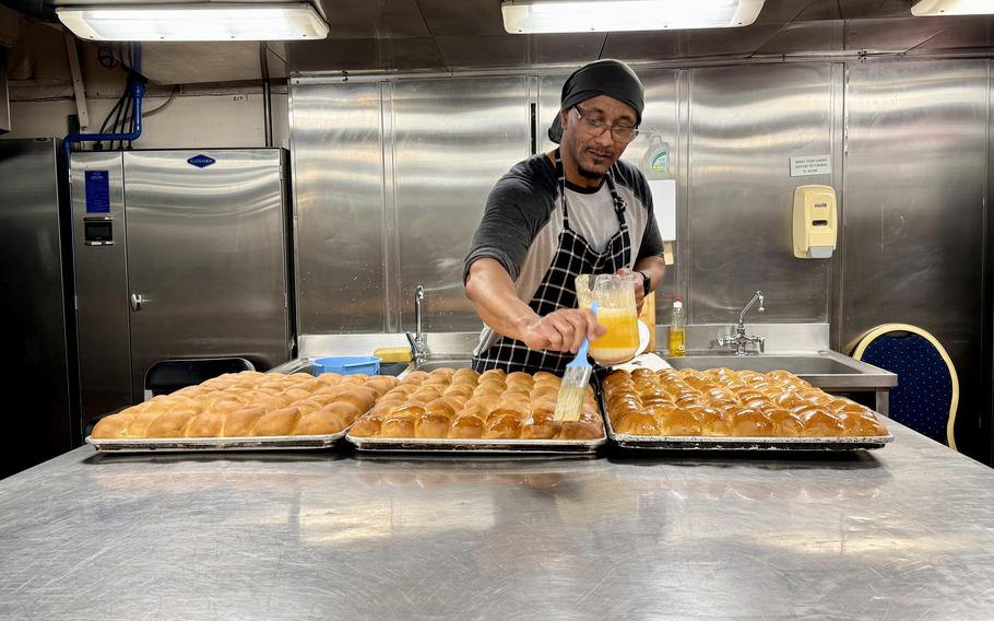 A man prepares bread in a kitchen aboard a ship.