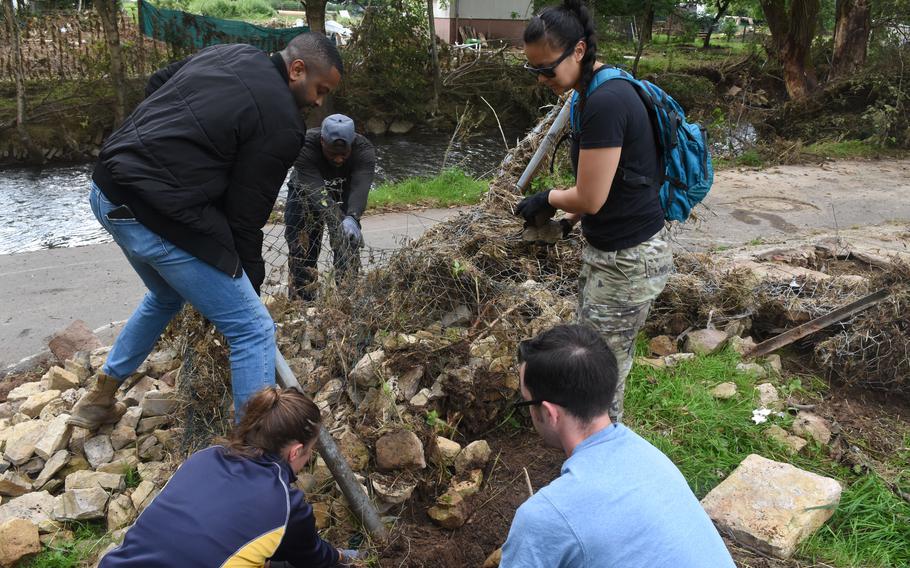 Airmen from Spangdahlem Air Base, Germany, work to untangle a metal fence from a pile of rocks that washed up on the banks of the Nims River in Rittensdorf, Germany, during the severe flooding in July 2021.