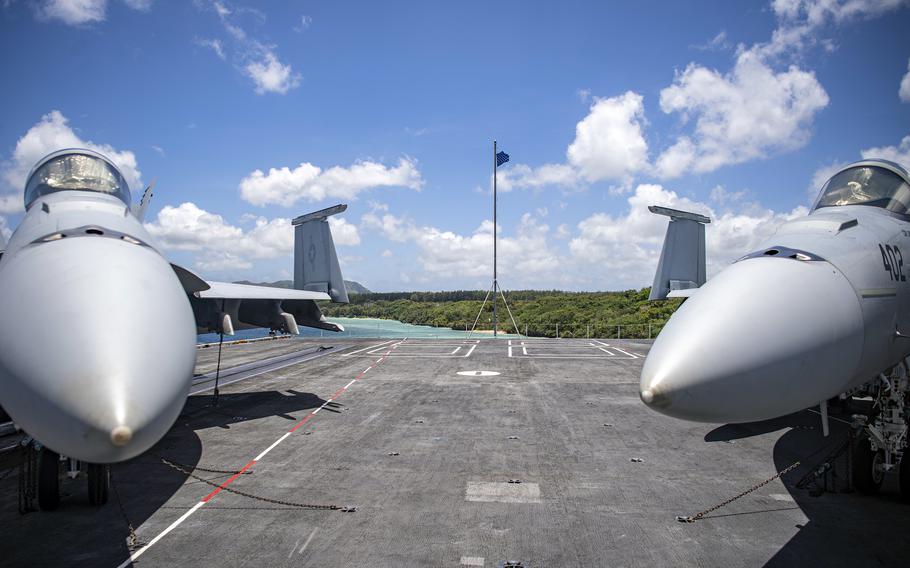 Military jets sit on the flight deck of a ship.