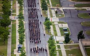 A large group of people in dark PT uniforms running in formation down a tree-lined street.
