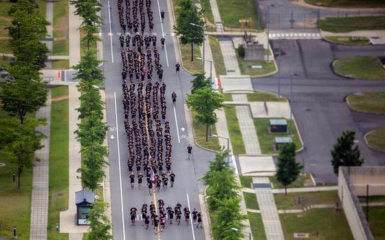 A large group of people in dark PT uniforms running in formation down a tree-lined street.