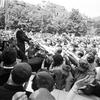 A black and white photo of a mass of people reaching their hands towards a Robert F. Kennedy. 